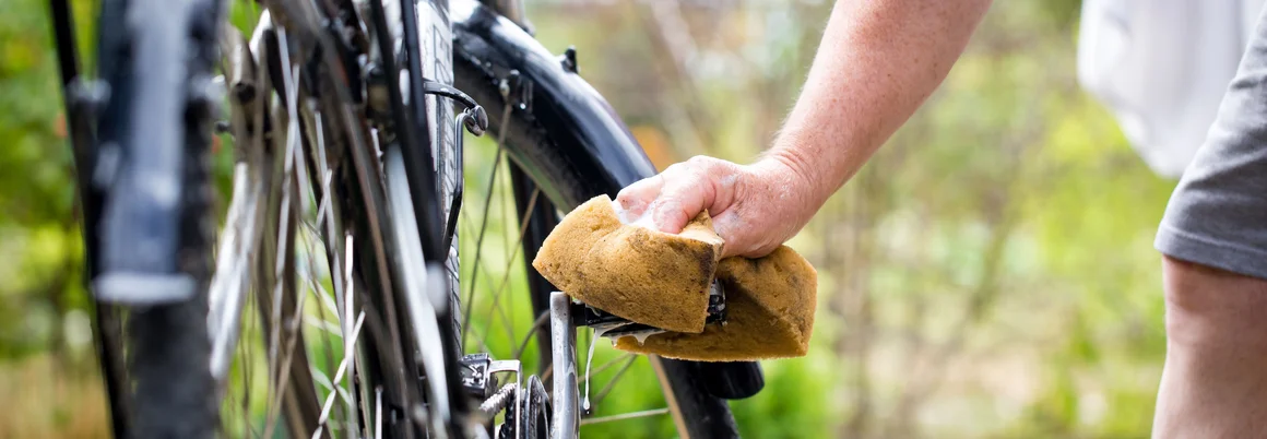 Person reinigt Fahrrad mit Schwamm.